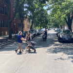 Person biking with cargo bike and family crossing street in foreground.